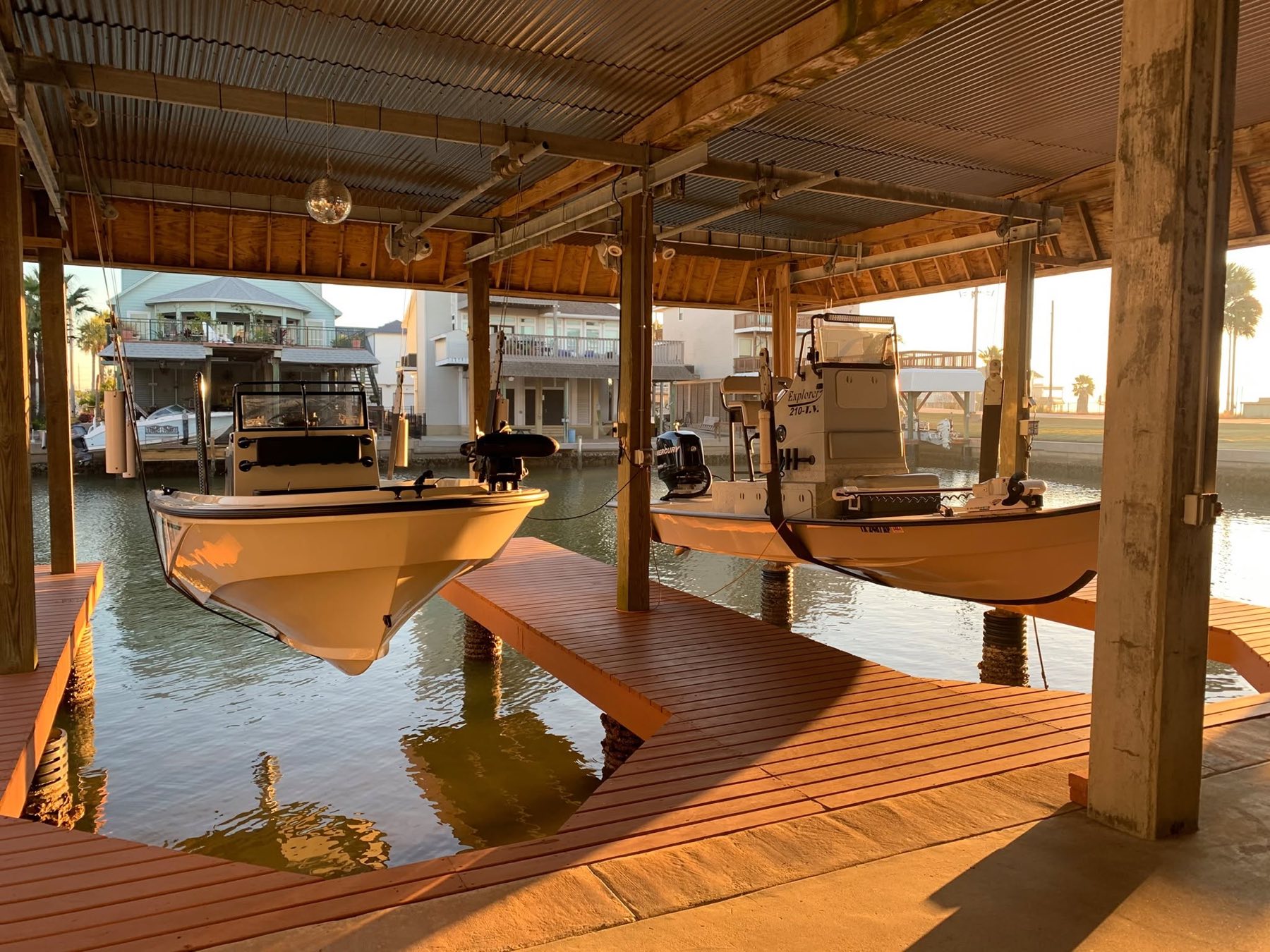 Two bay boats on lifts under a covered dock at sunrise