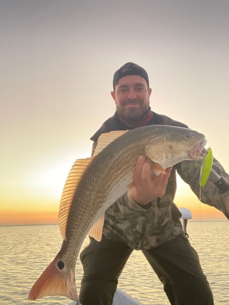 Capt. James Harrelson holding a redfish on the bow at sunrise over Galveston Bay