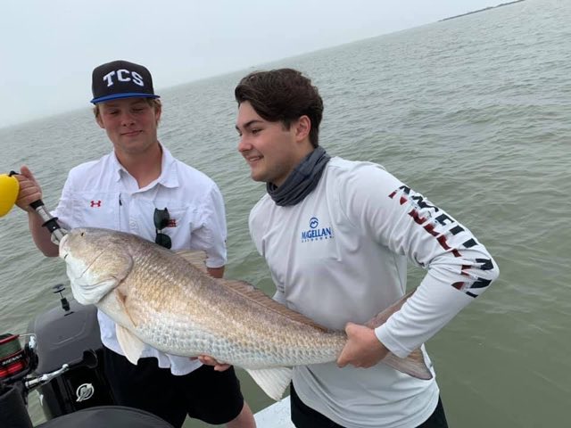 Two anglers holding a big redfish on the boat