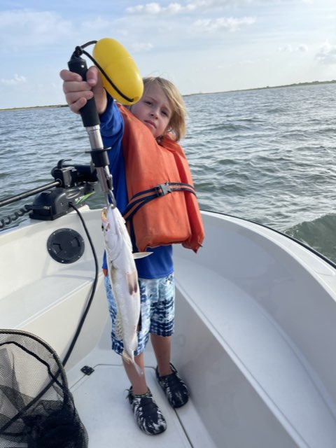 Young angler in a life jacket holding up a trout