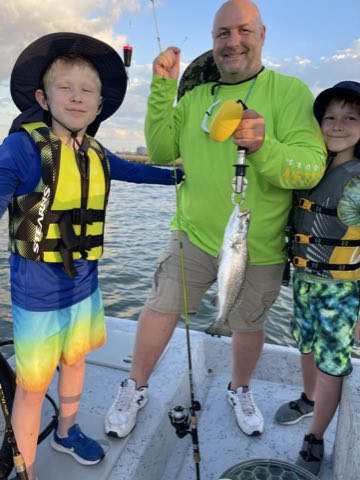 Angler in a green shirt with two young anglers and a speckled trout