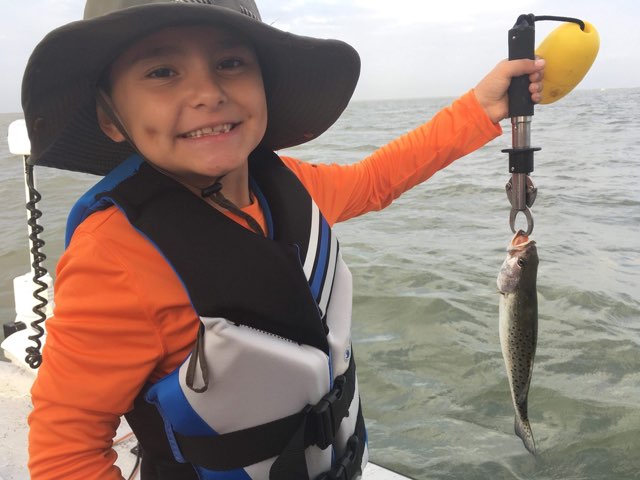 Young angler in a sun hat holding up a trout