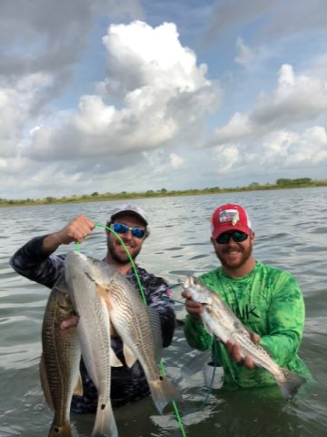 Two wading anglers holding up big redfish