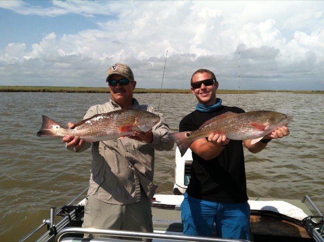 Two anglers each holding a redfish on the boat