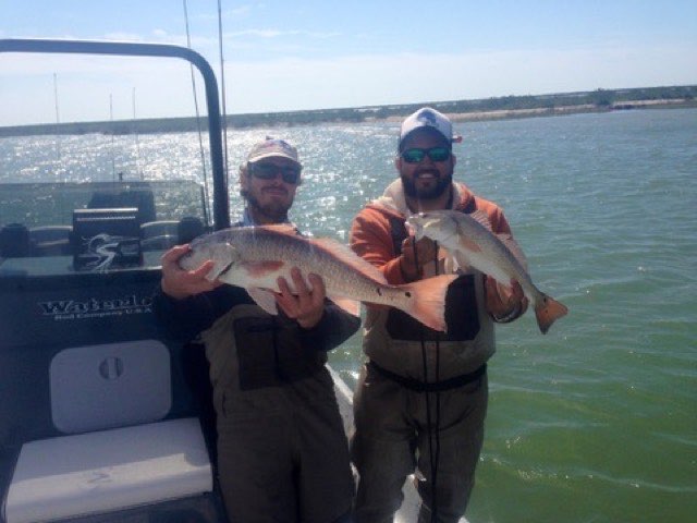 Two anglers holding redfish on the boat