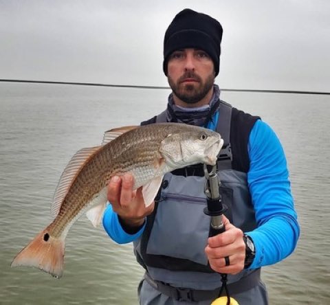 Angler in a beanie and waders with a redfish