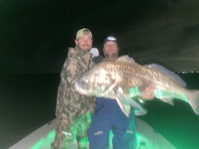 Two anglers with a big black drum at night