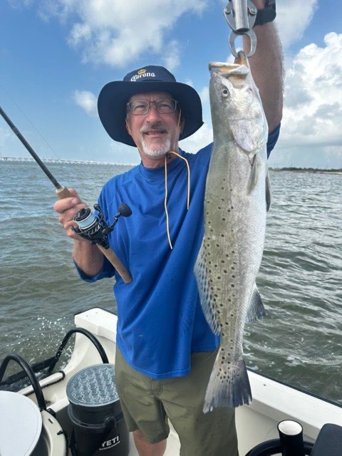 Angler in a sun hat holding up a speckled trout