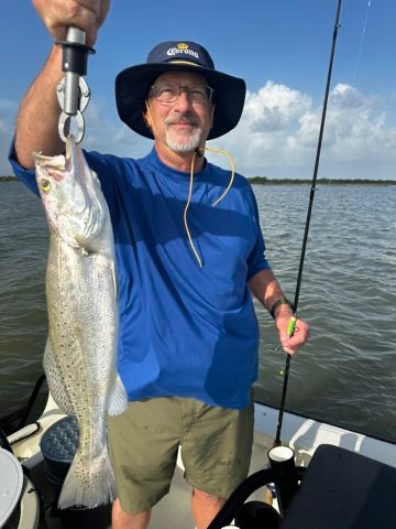 Angler in a sun hat holding up a big speckled trout on the scale