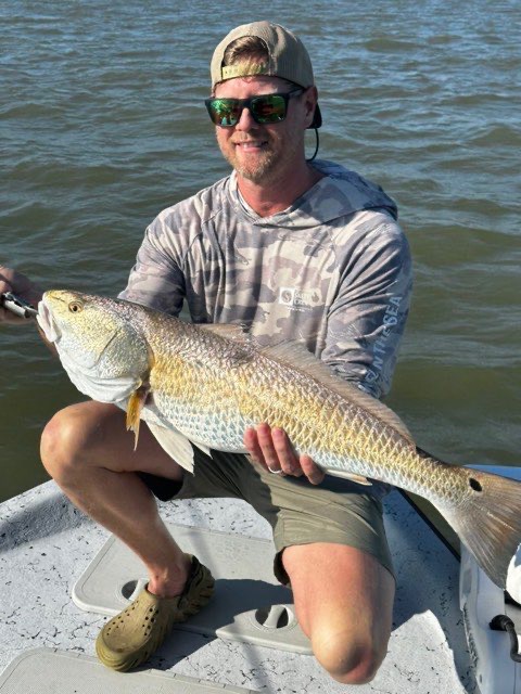 Angler kneeling on the deck with a redfish