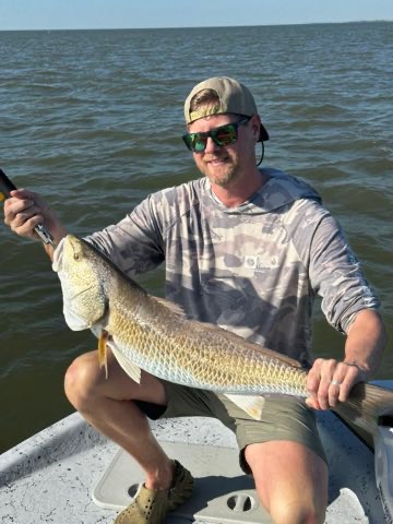 Angler kneeling on the deck with a big redfish