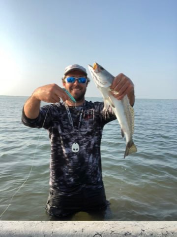 Wading angler with a speckled trout caught on topwater